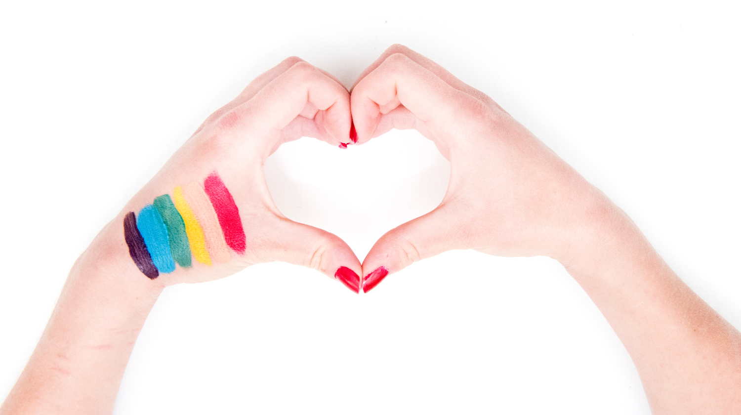 Två händer formar ett hjärta, ena handen har en målad prideflagga.